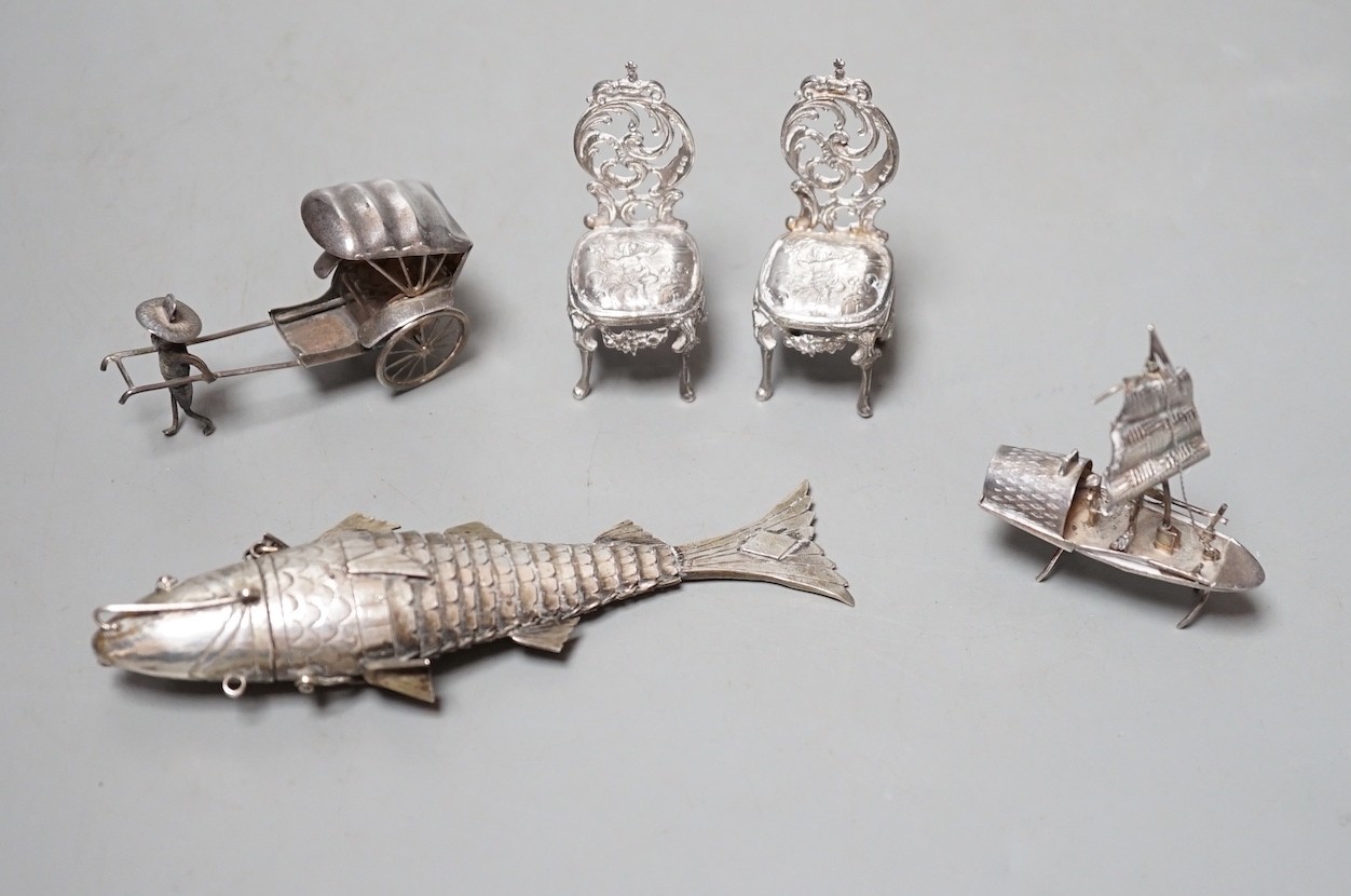 A pair of miniature white metal occasional chairs, a sterling rickshaw and boat and an articulated fish pill box.